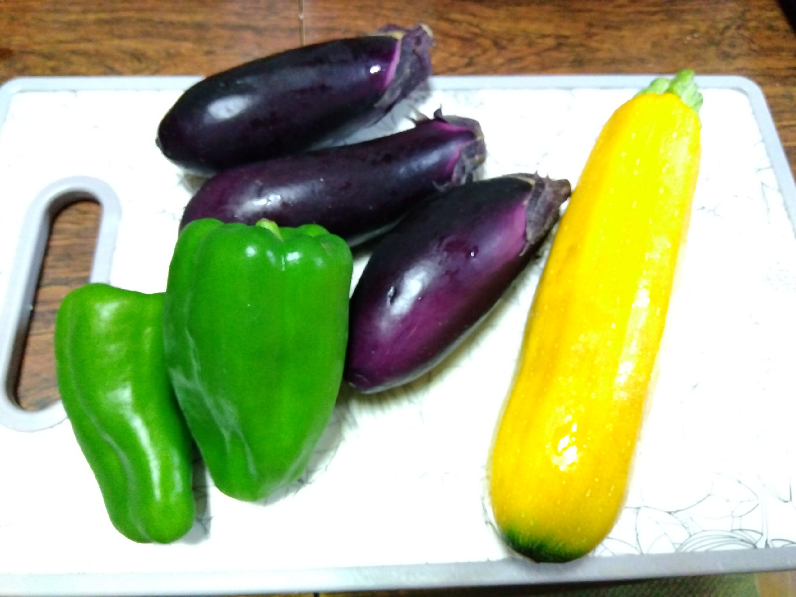 まな板の上に並んだ夏野菜のナス、ピーマン、黄色いズッキーニ