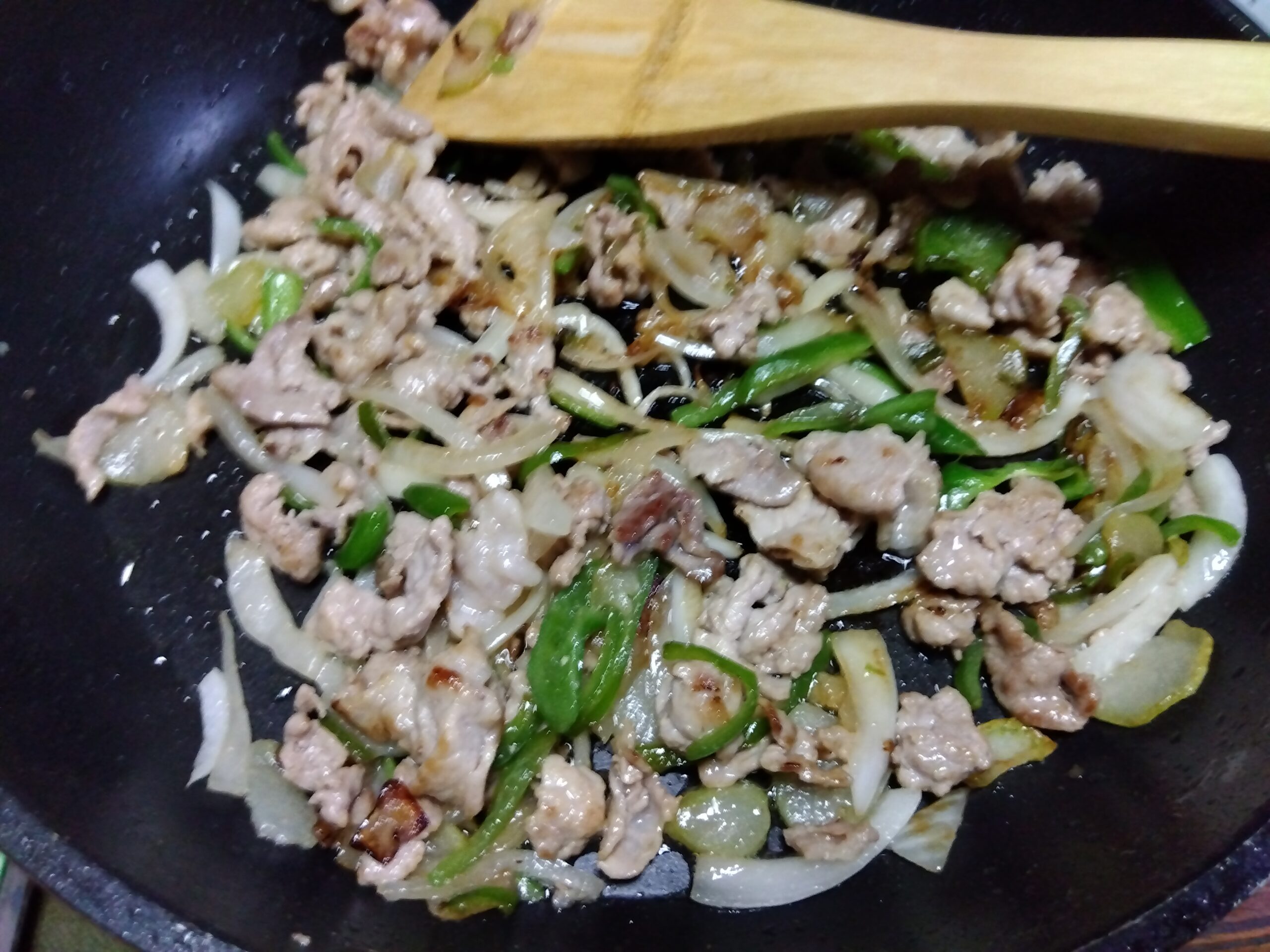豚肉、タマネギ、ピーマン、ニンニクを炒めている