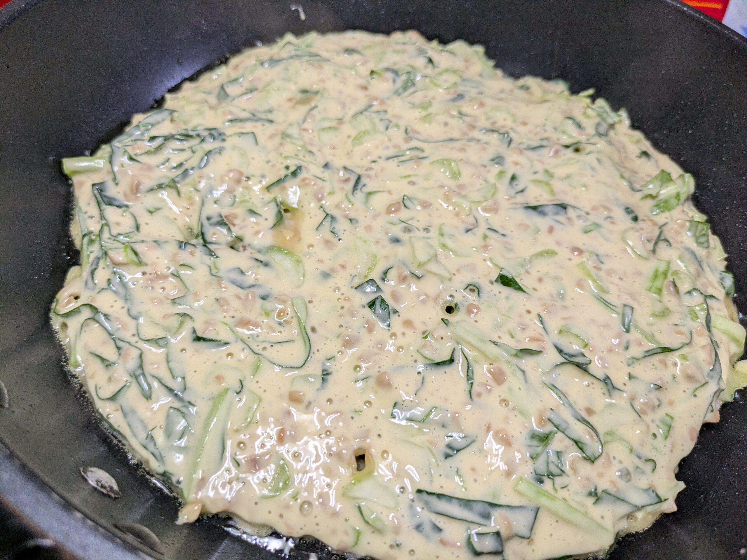 焼き始めた小松菜と納豆、豚小間肉のお好み焼き