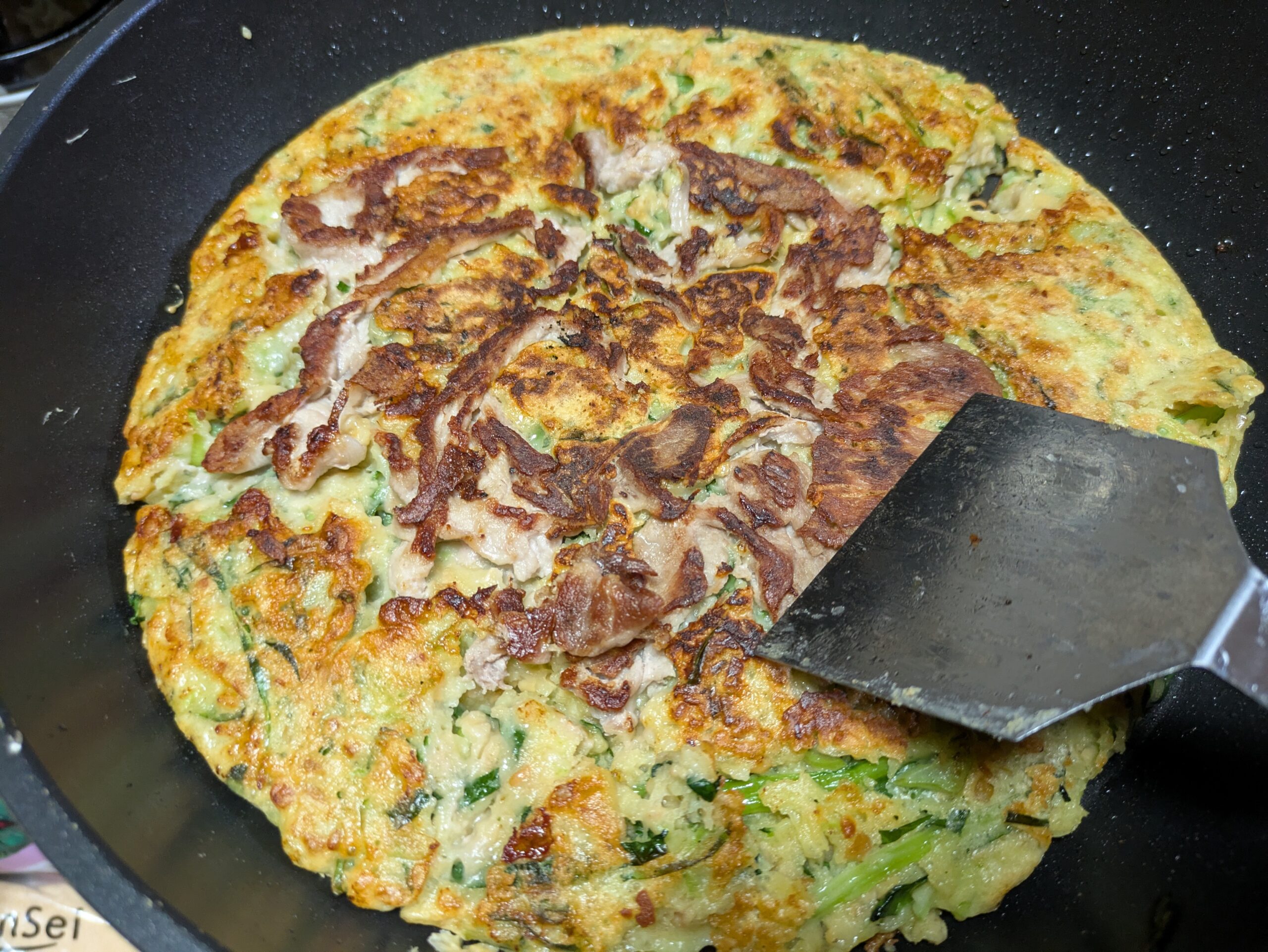 ひっくり返して焼き色のついた小松菜と納豆、豚小間肉のお好み焼き