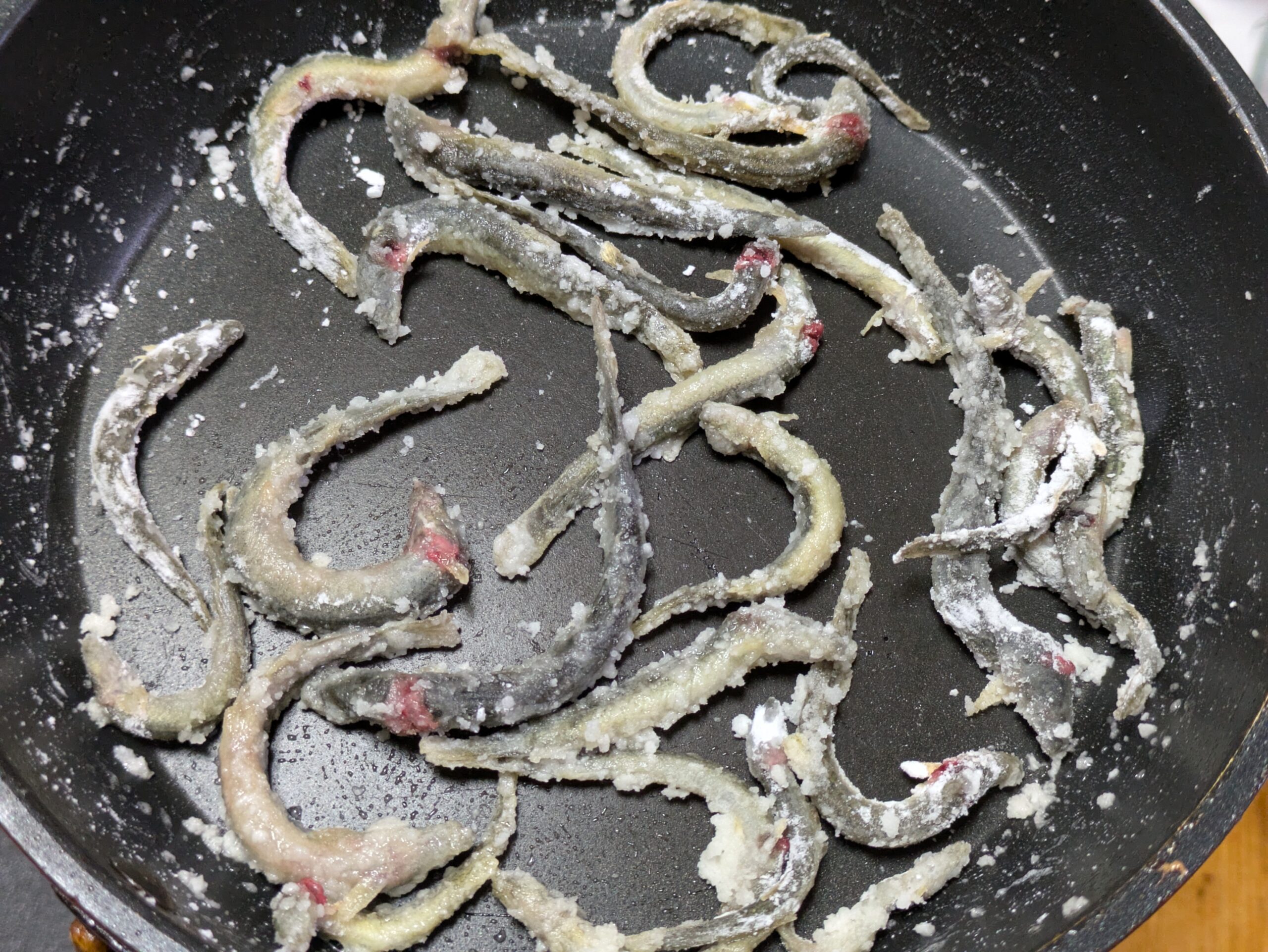 片栗粉をまぶした丸ごとのドジョウをフライパンで焼いているところ