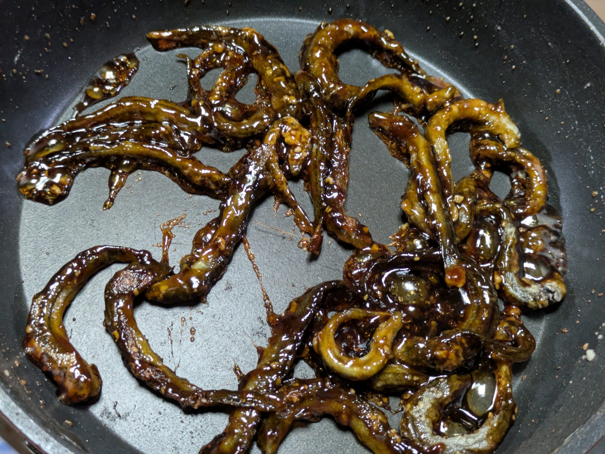 甘辛いかば焼きのタレを丸ごとのドジョウへ絡めているところ
