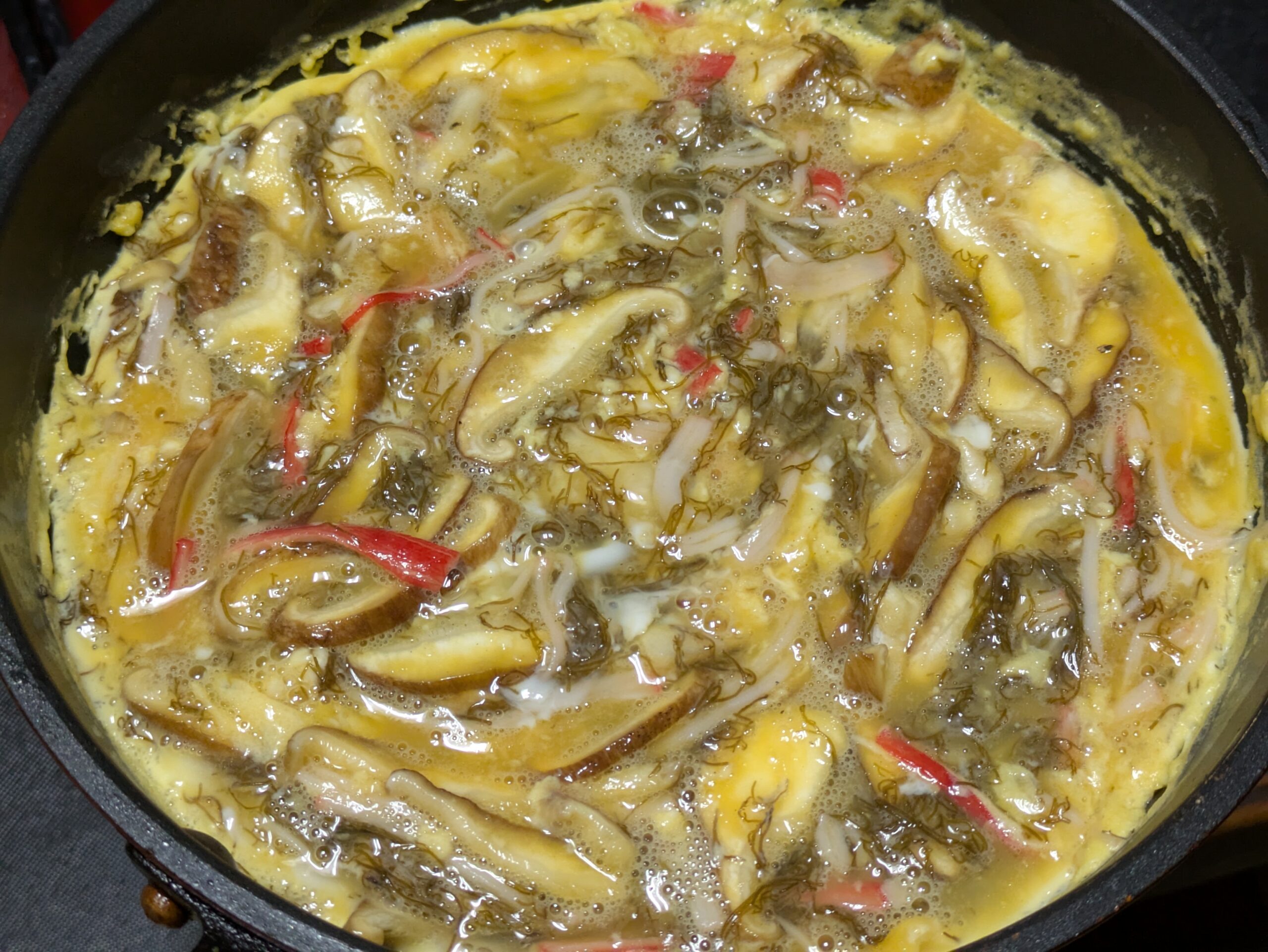 もずくと椎茸とカニカマ入りの卵をフライパンで焼いている様子
