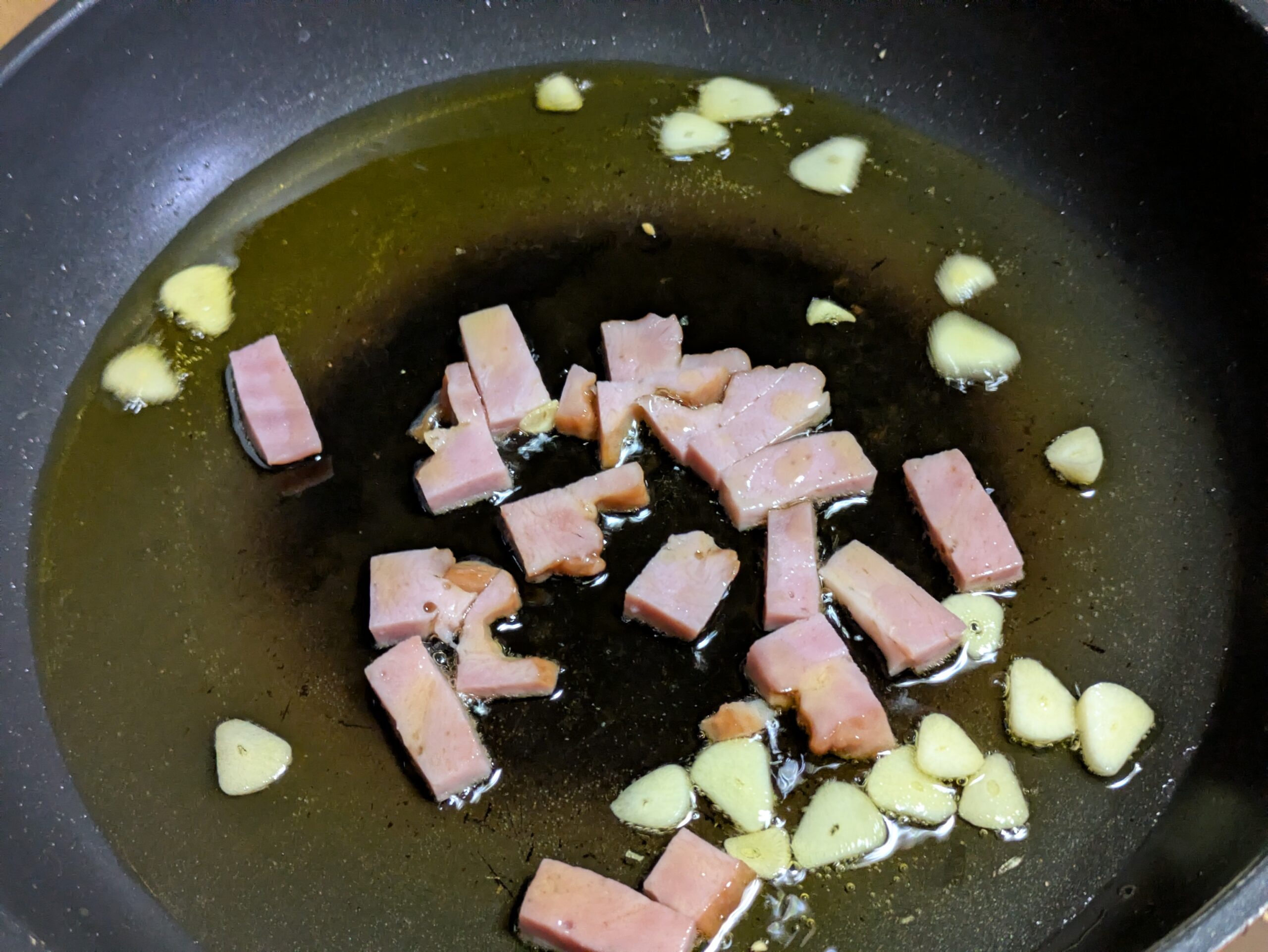 オリーブオイルでにんにくとベーコンを炒めている様子