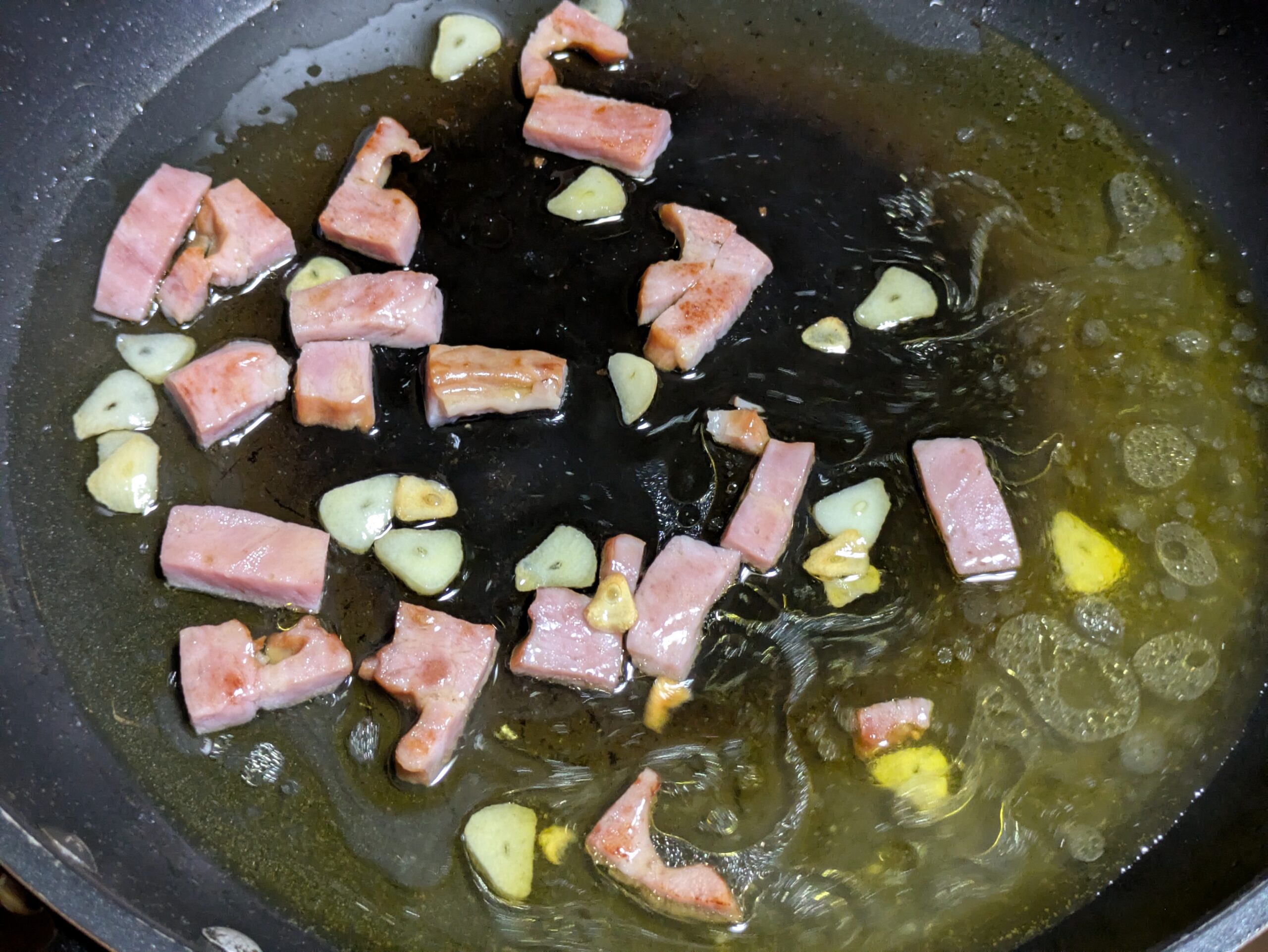 フライパンに茹で汁を加えてベーコンとにんにくをなじませている様子