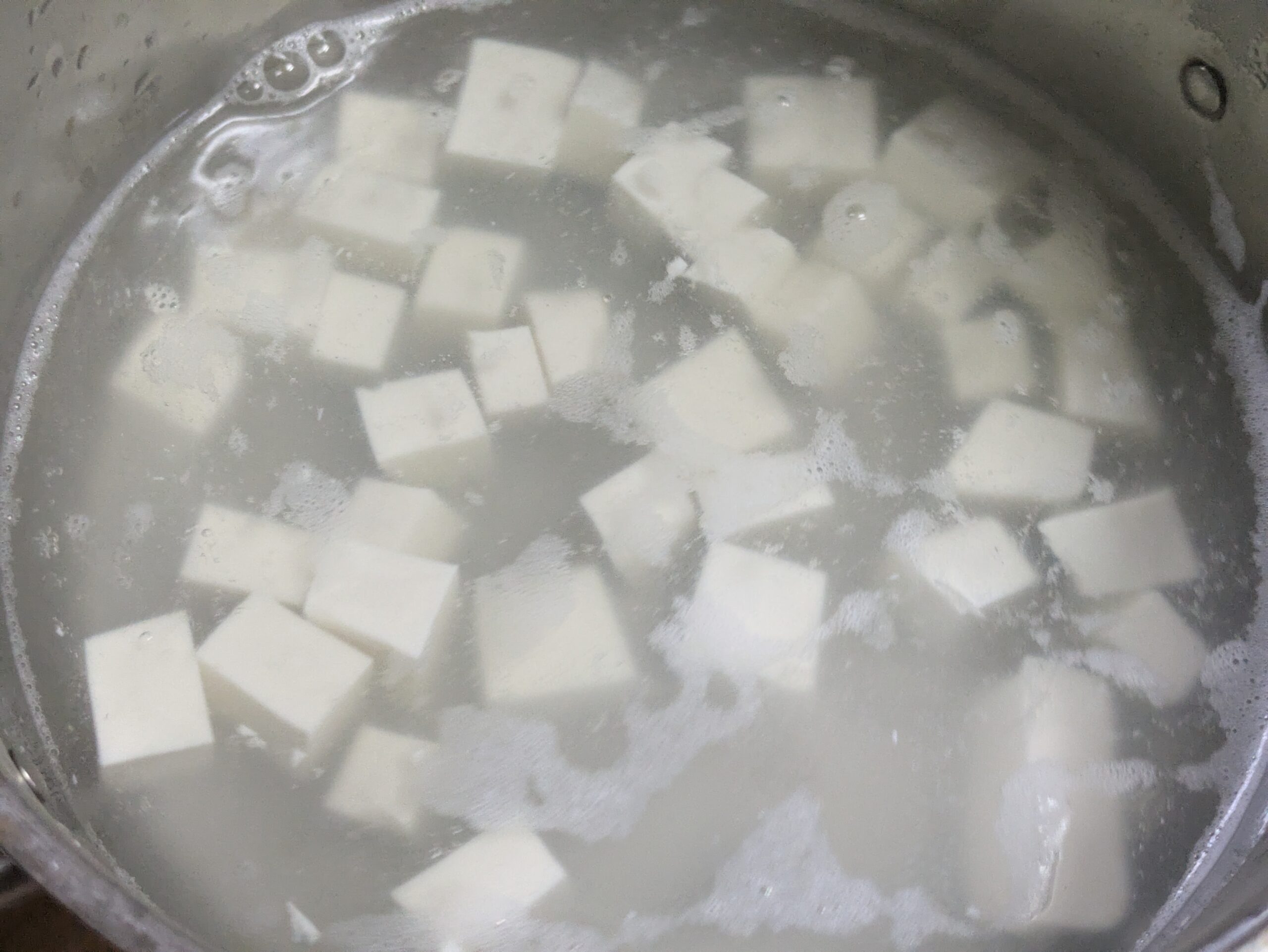 鍋のスープにさいの目切りの豆腐を入れて温める様子
