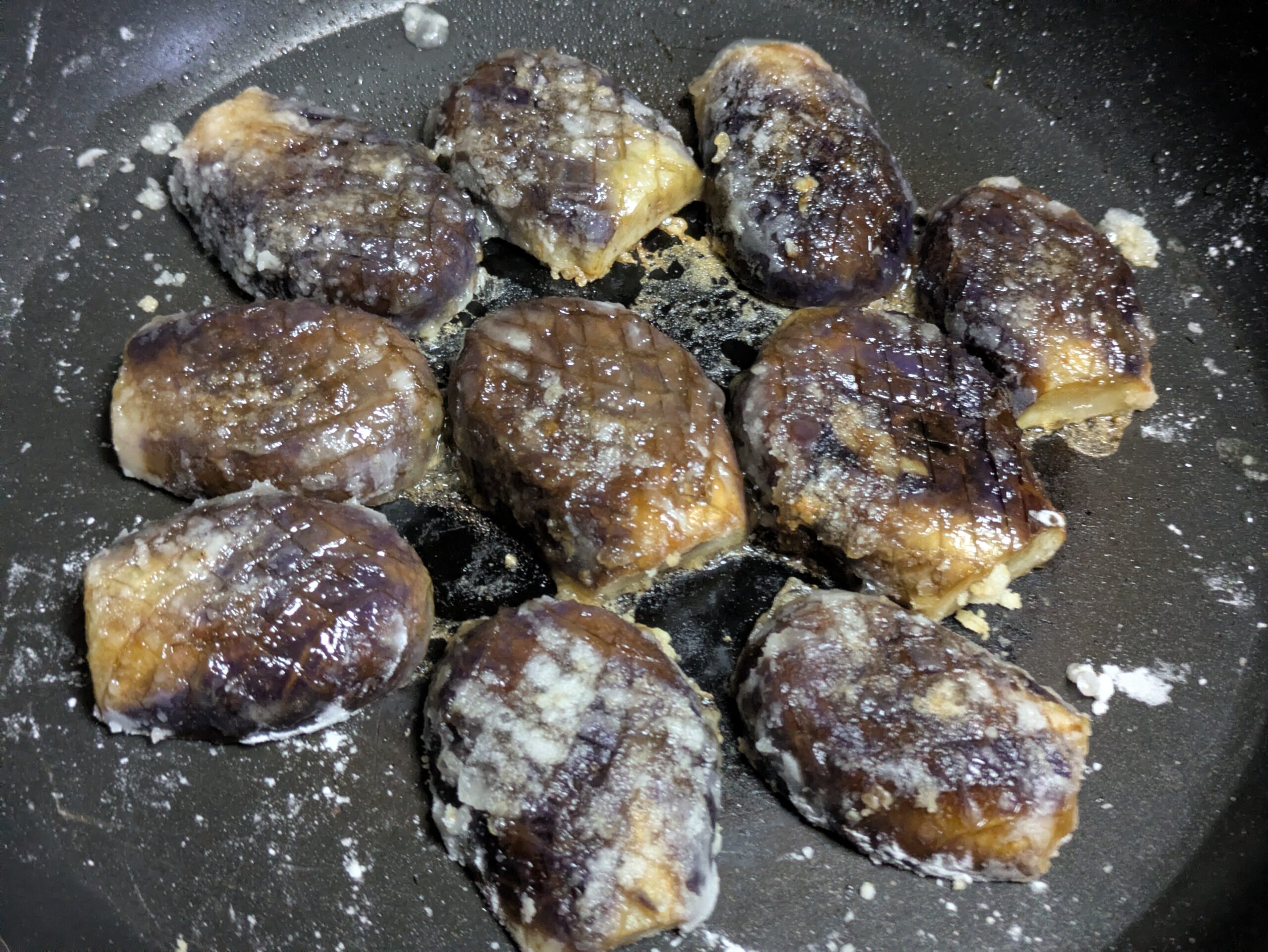 柔らかく焼けたヘタ紫なすをフライパンで押して平たくしている様子