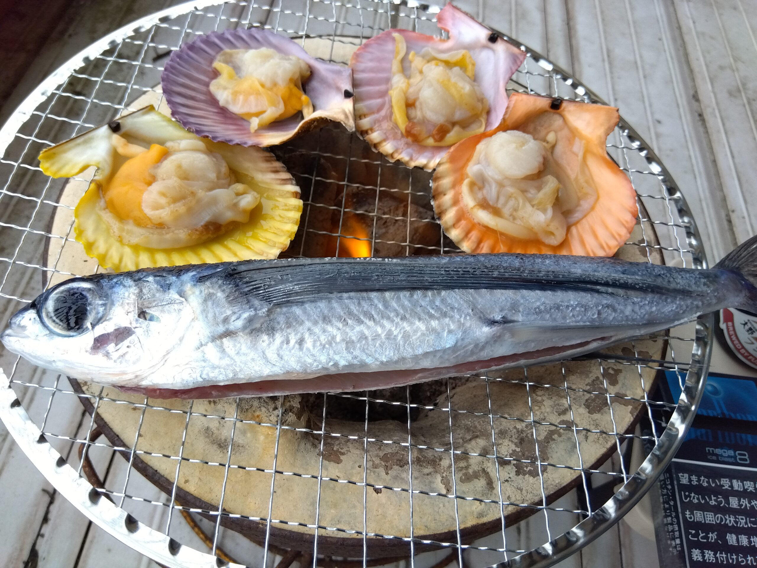 七輪の上で焼かれるトビウオとカラフルなヒオウギ貝