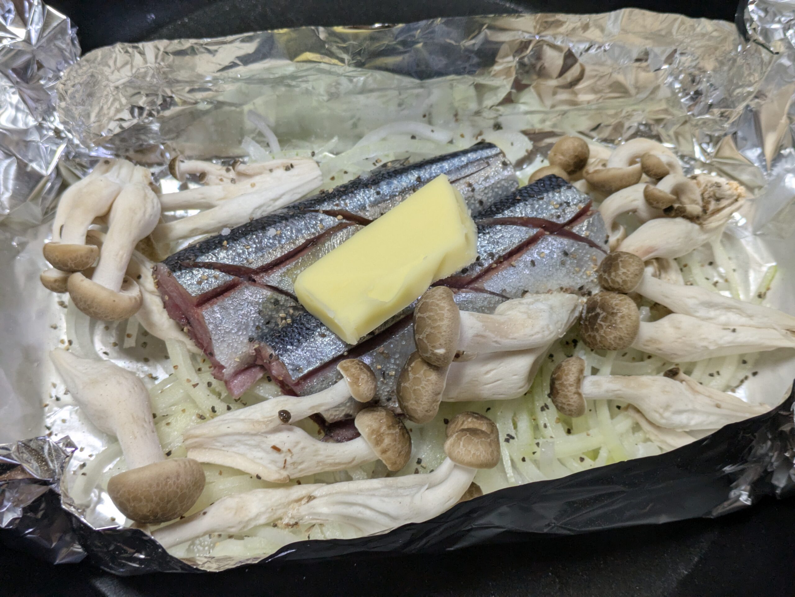 アルミホイルに玉ねぎとサンマとしめじを並べてバターをのせたところ