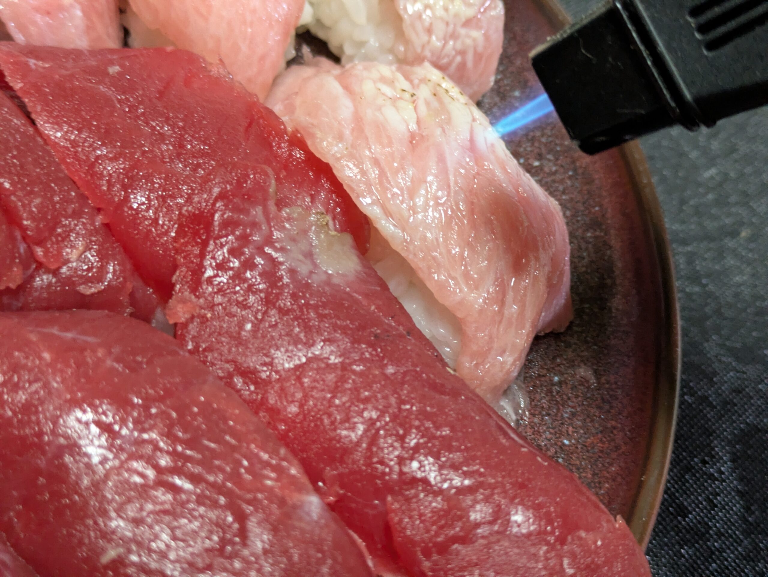 料理用バーナーでマグロのトロ寿司を炙っている様子