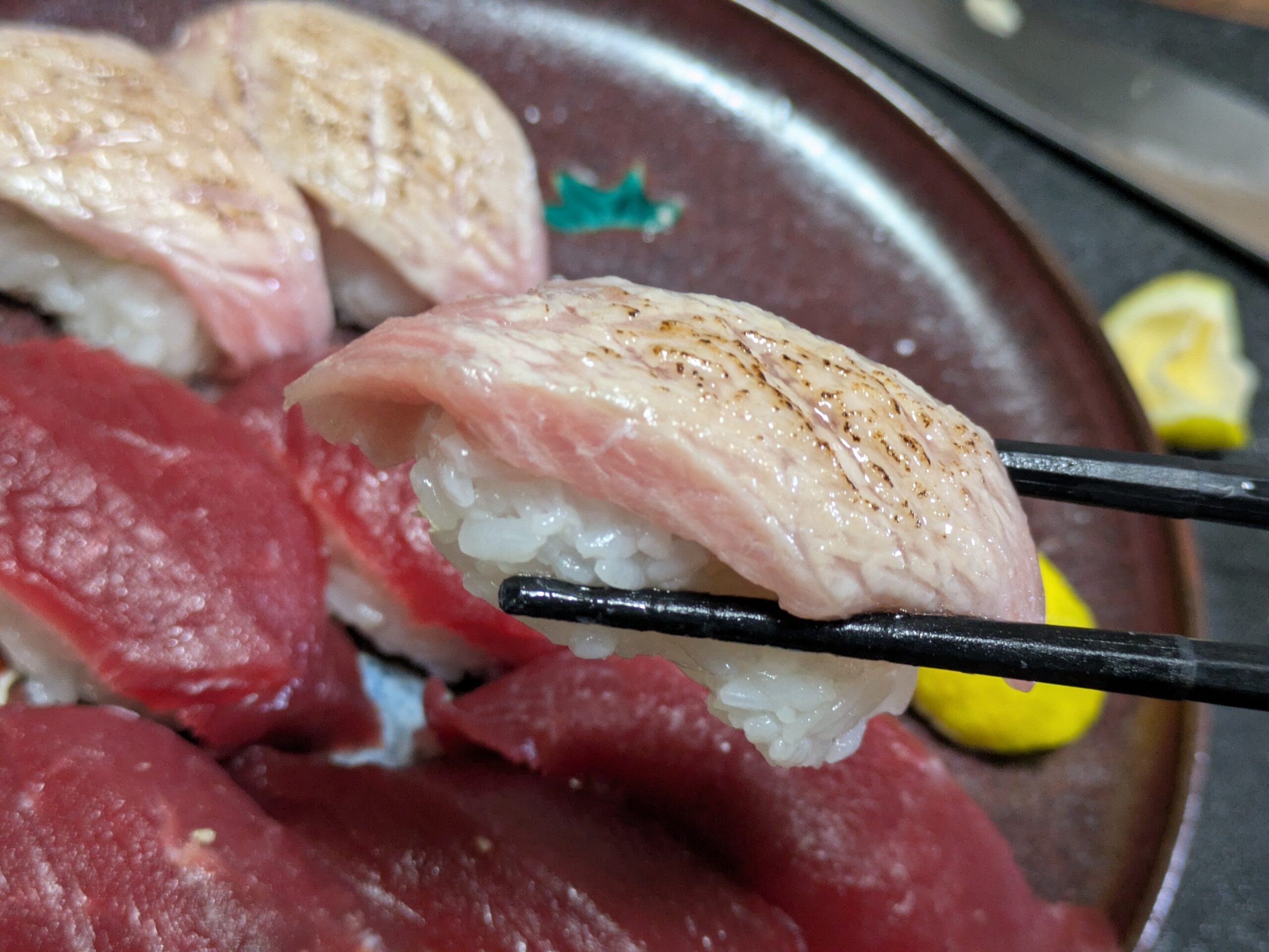 箸で持ち上げた柚子果汁をかけた炙りトロの握り寿司