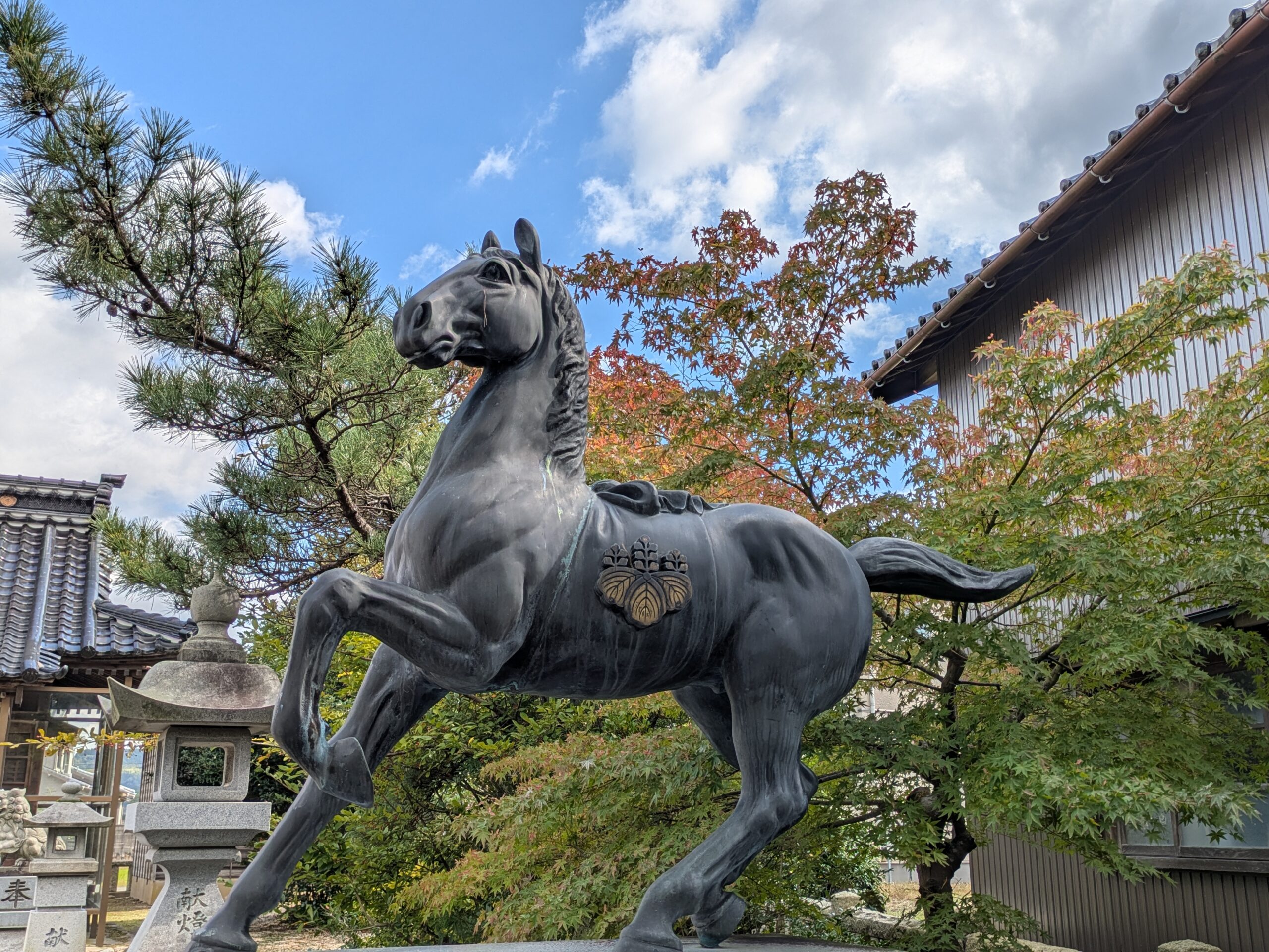 忠縄神社にある前脚を高く上げた馬の像と背景の色づき始めたモミジ
