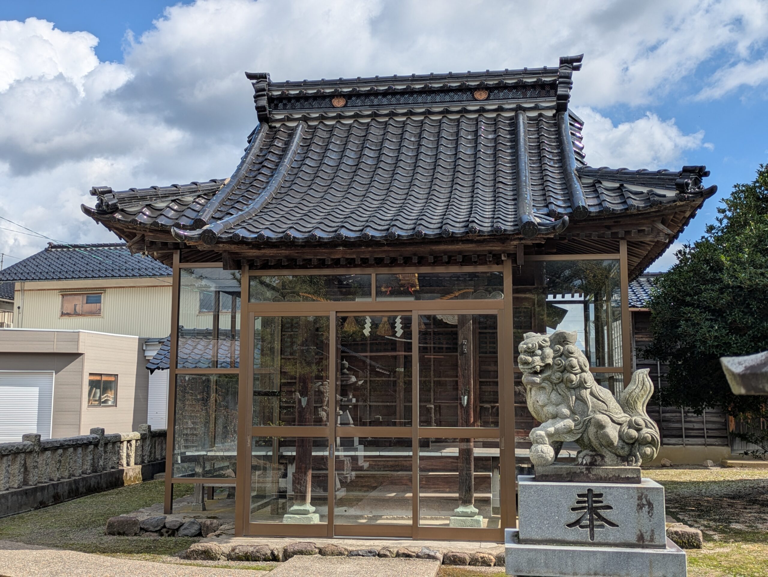 ガラスサッシで覆われた忠縄神社の拝殿と手前の狛犬
