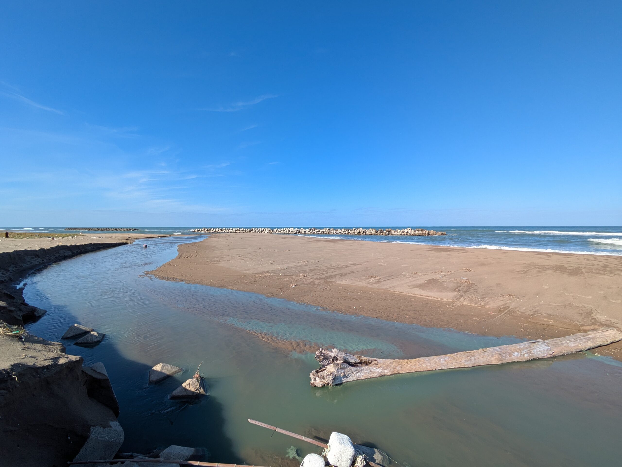 相川新町の河口で青白く見える水と砂地に残された流木